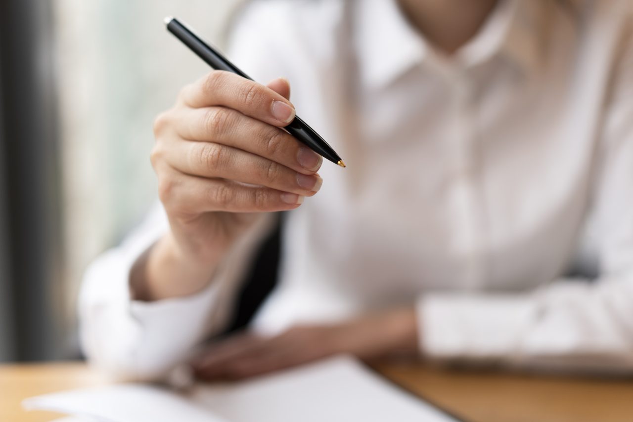 mulher de camisa branca segurando caneta preta para responder prova