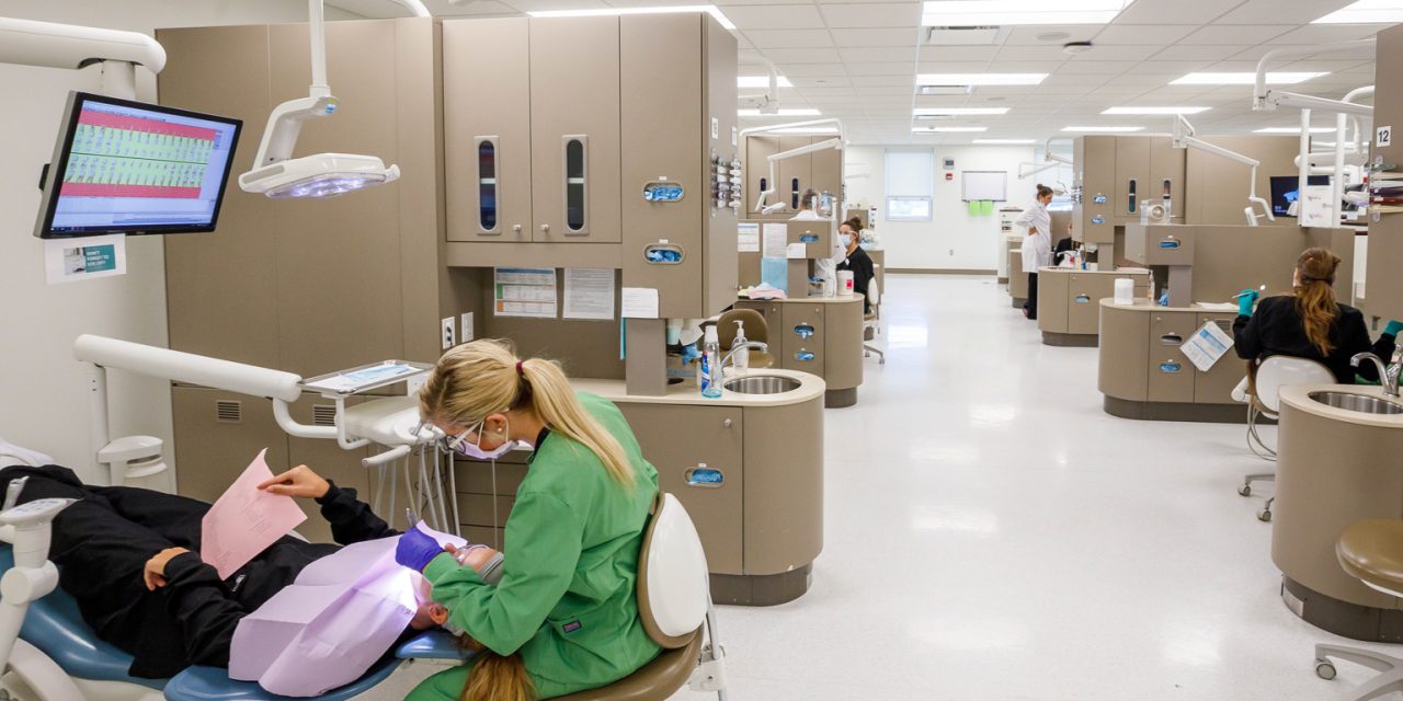 Clínica escola de odontologia tem vários consultórios abertos um ao lado do outro e pacientes sendo atendidos.