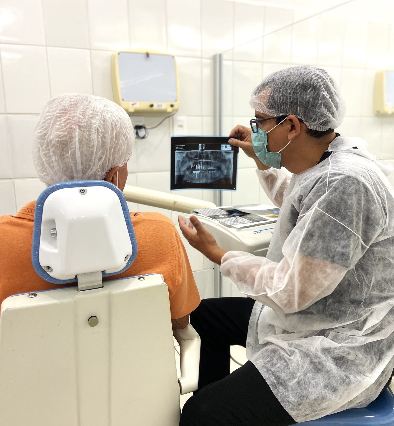 Aluno da EAP Goiás na clínica escola de odontologia está explicando procedimento para paciente mostrando os problemas no raio-x.