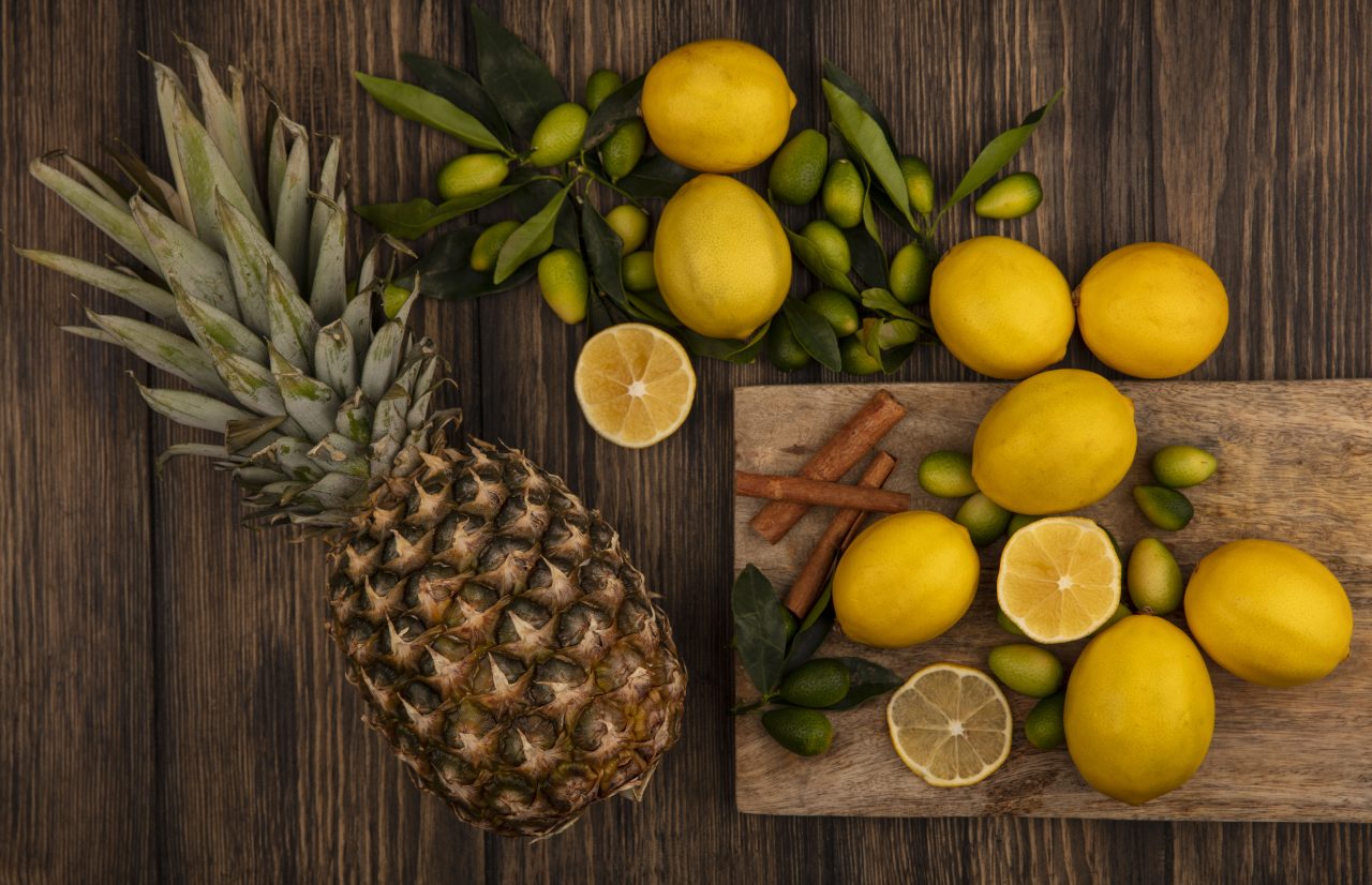 Mesa de madeira tem frutas ácidas em cima. Como abacaxi, laranja e limão.