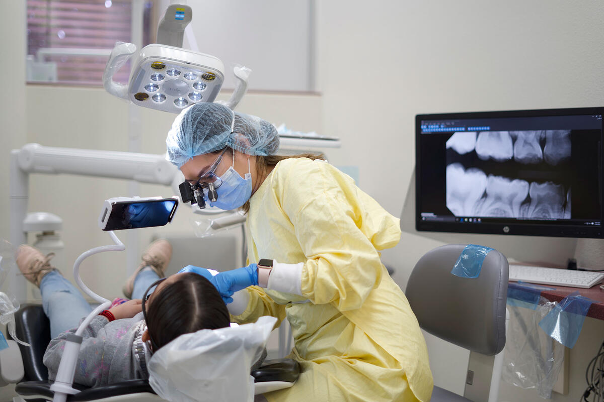 Dentista fazendo avaliação de dentes de paciente; Na tela, tem um raio-x de dentes.