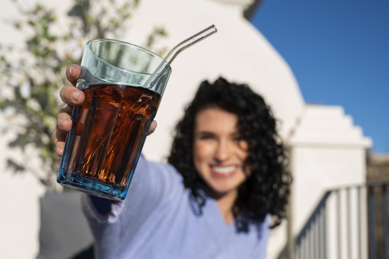 Mulher sorrindo e segurando um copo de vidro com refrigerante dentro