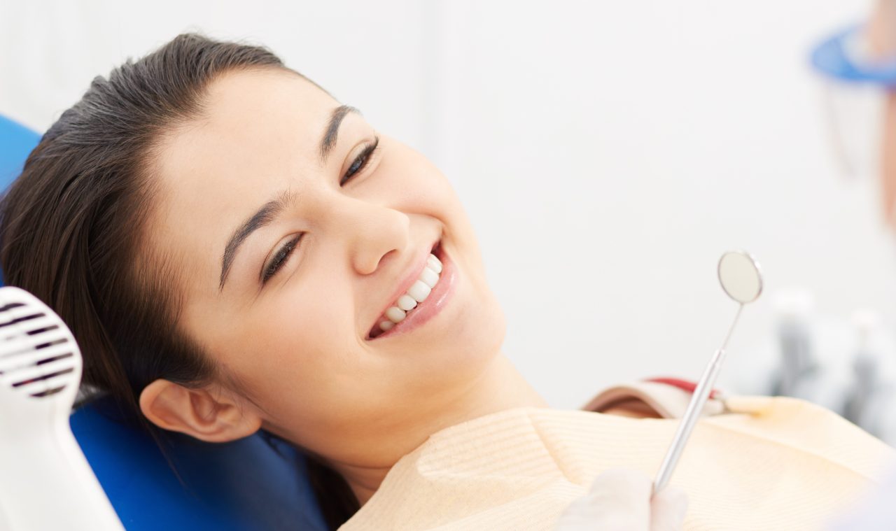 Paciente mulher no dentista, ela está na cadeira odontológica e sorrindo.