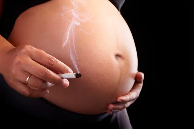 Mulher grávida está segurando um cigarro aceso ao lado da barriga.