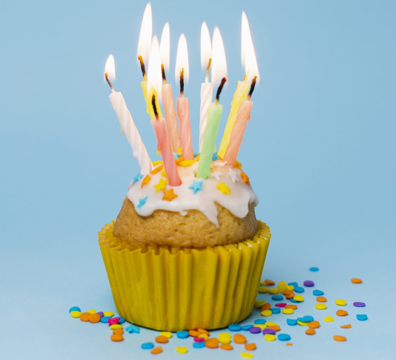 Cupclae com sainha amarela, confetes em forma de estrela e várias velas de aniversário acesas.