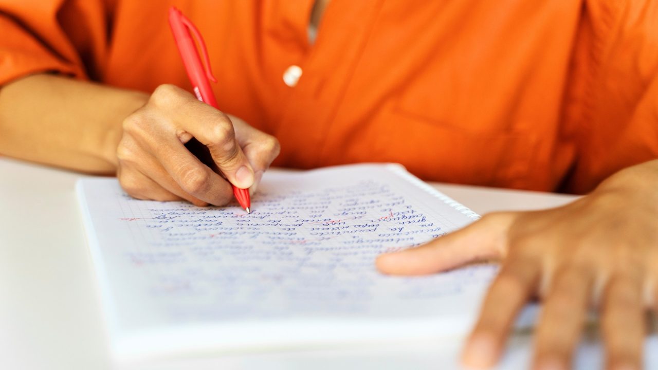 Mulher está corrigindo um trabalho feito em papel almaço.
