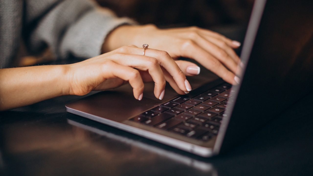 Mulher com anel de noivado digita em seu notebook.