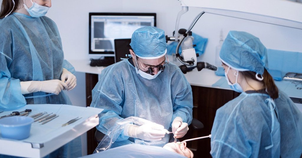 Três dentistas realizando procedimento em paciente no consultório.