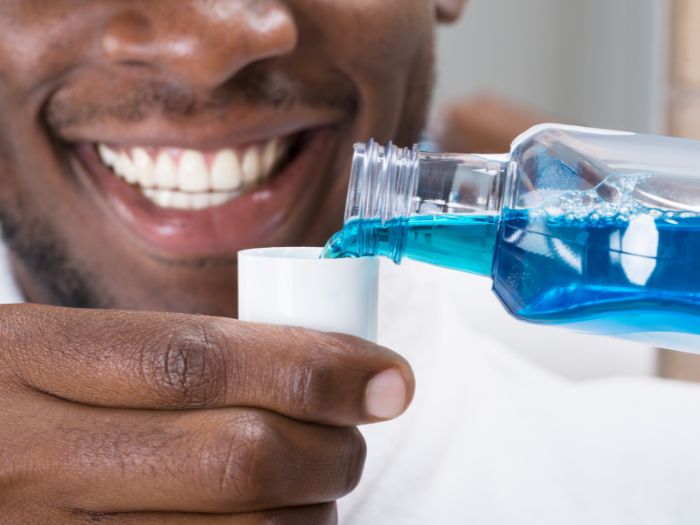 Homem sorrindo está colocando enxaguante bucal na tampinha.