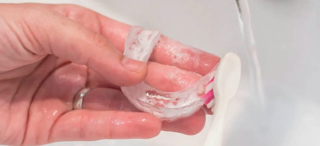 limpando a placa de bruxismo com escova de dentes na pia