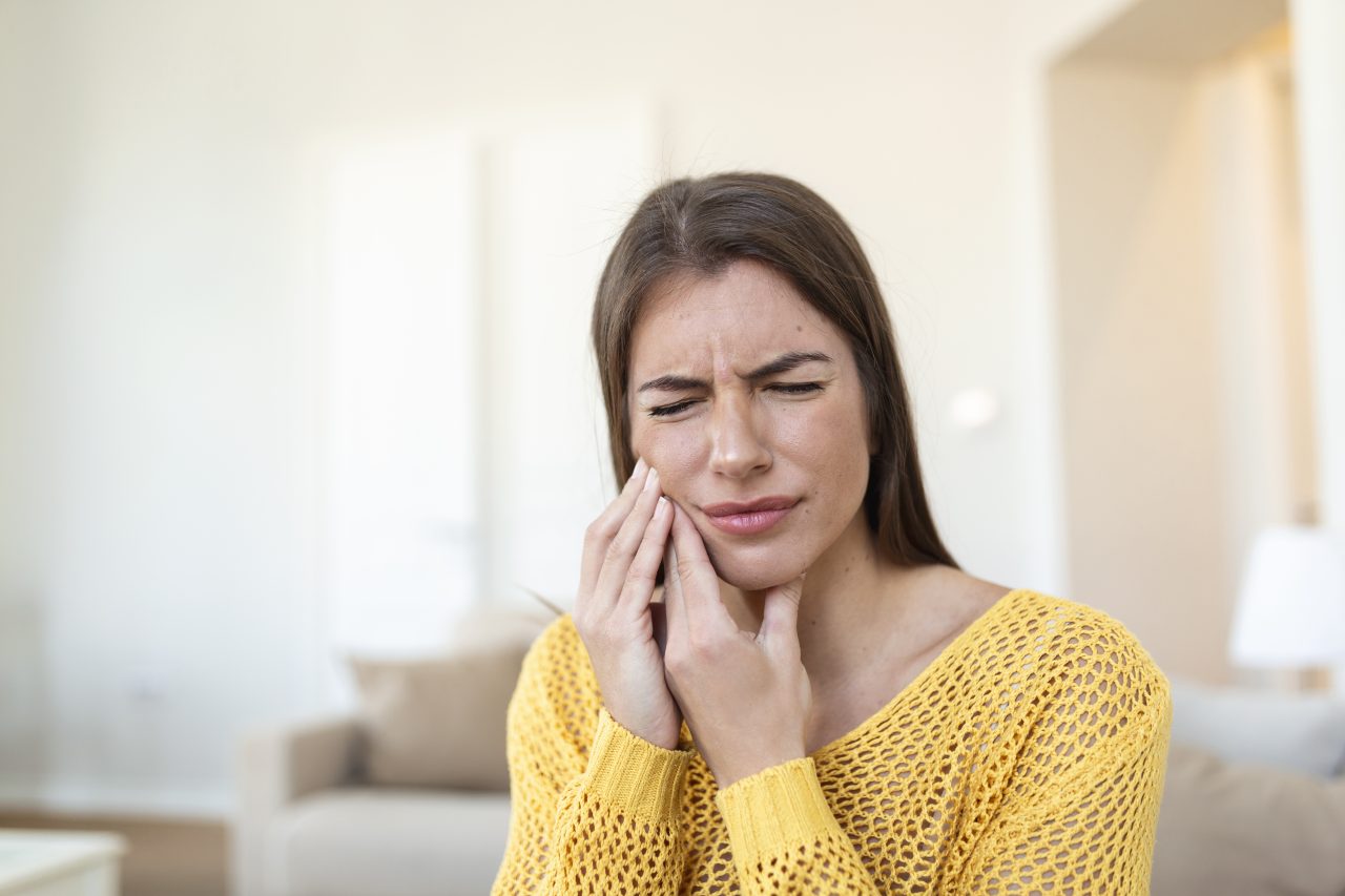 Mulher jovem com dor de dente, ela está em casa, no sofá, com a mão apoiada na bochecha