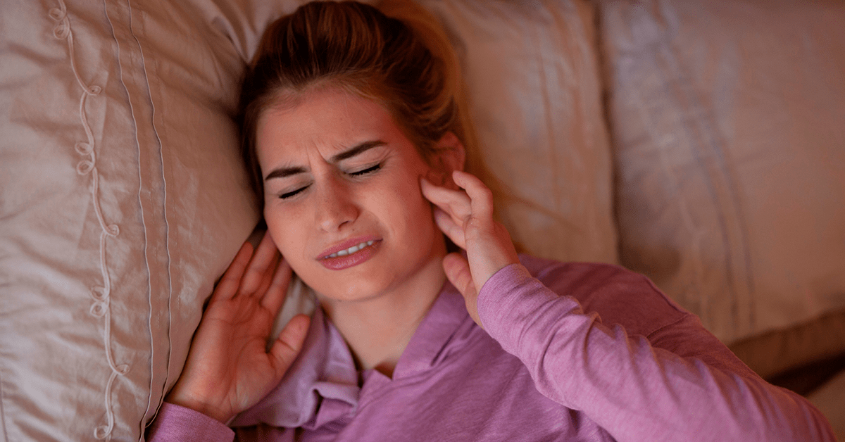 mulher deitada na cama está com dificuldade para abrir a boca e faz massagem na mandíbula