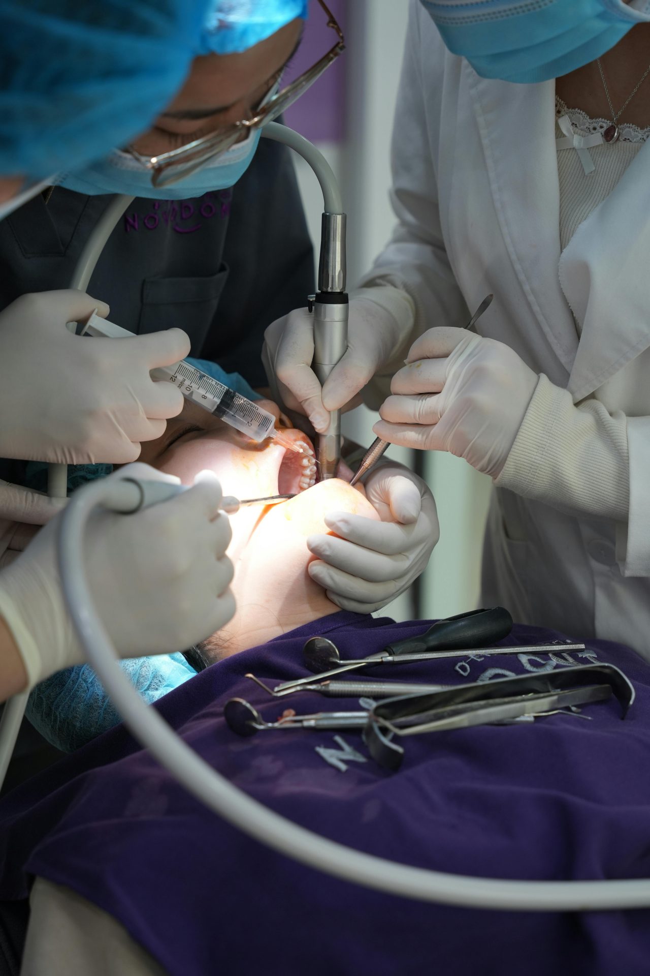Dentista e assistentes realizando procedimento em paciente. A dentista está segurando um anestesia.