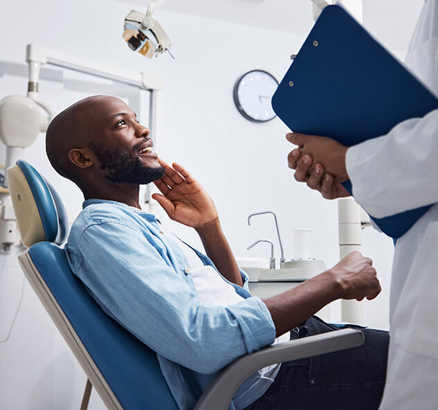 paciente conversando com dentista que está em pé ao seu lado segurando uma prancheta