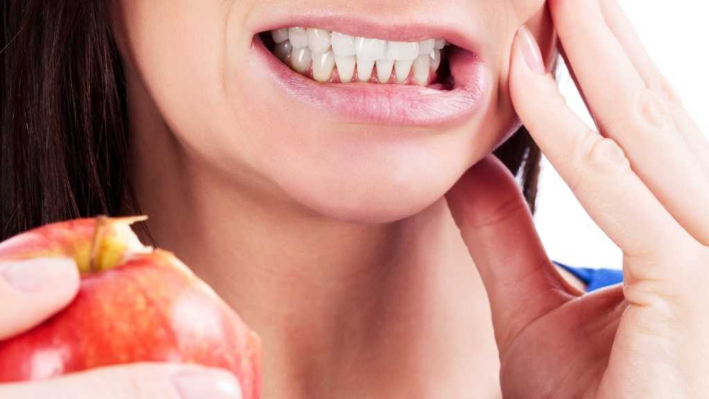 Mulher morde maça e sente dor.