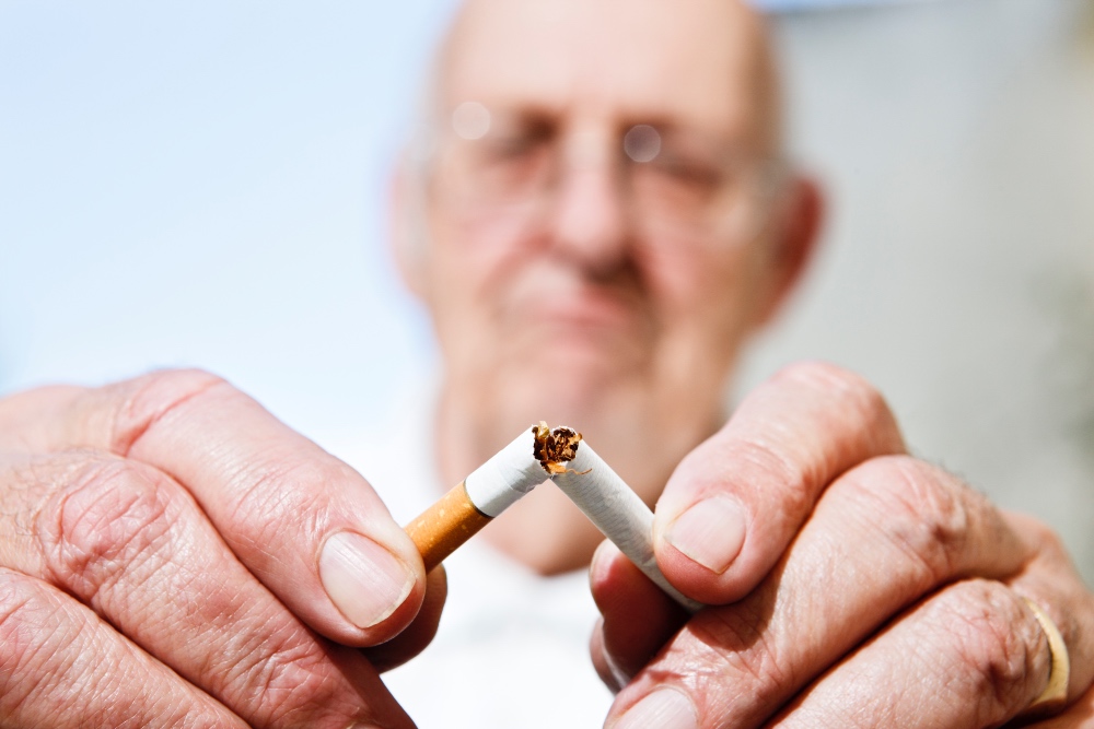 Senhor idoso com expressão de desgosto está partindo cigarro ao meio.