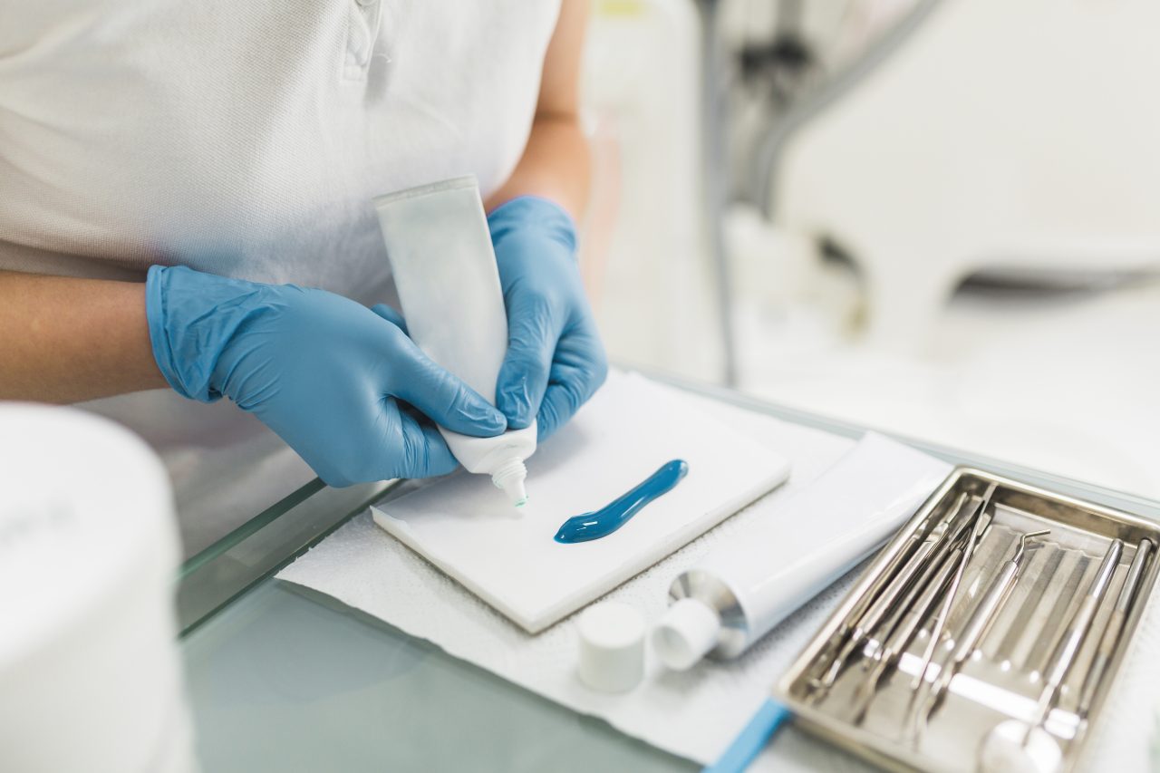 Dentista está preparando seus instrumentos antes de paciente chegar. Ela está despejando um líquido em cima de um papel.