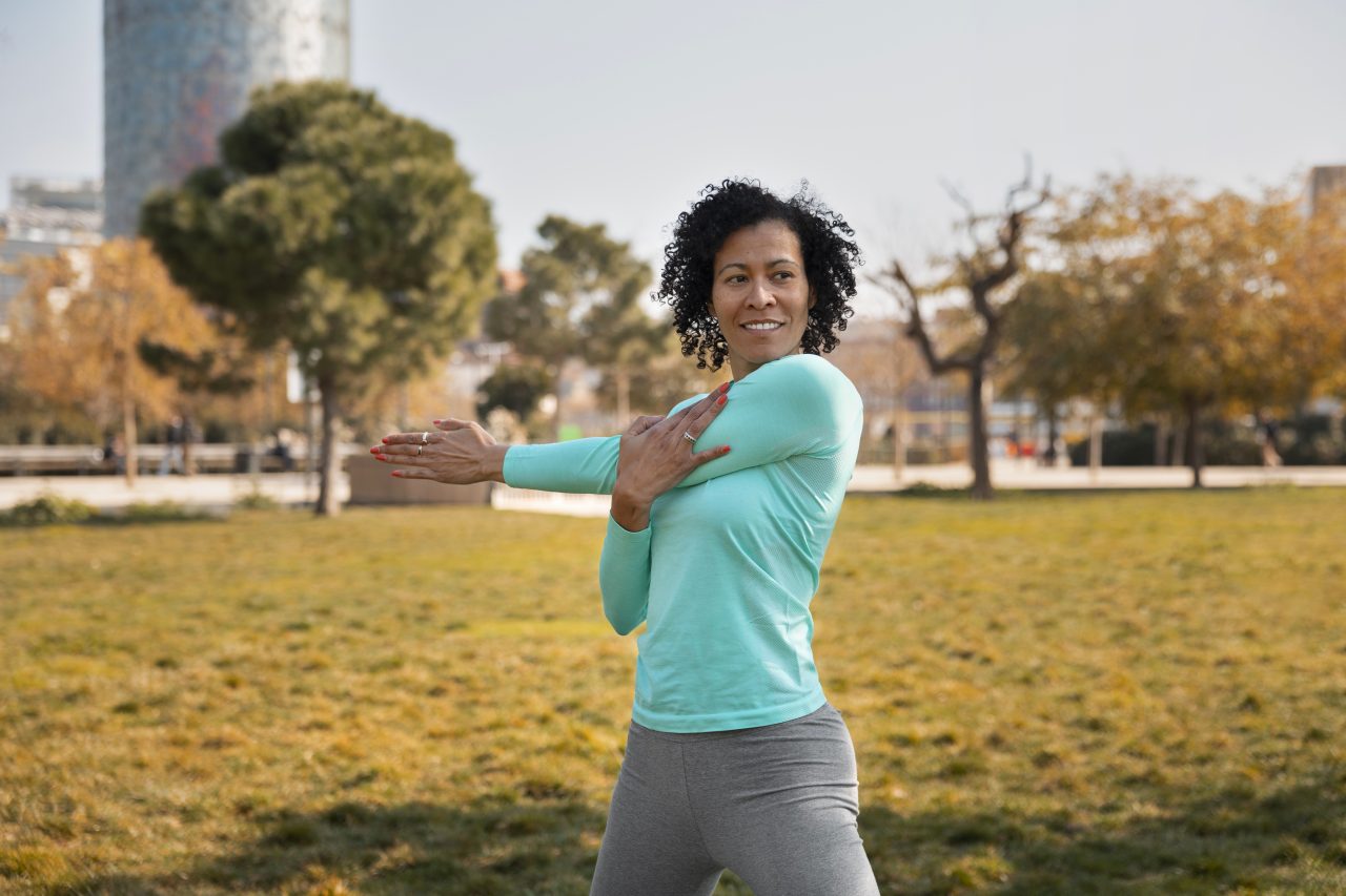 Mulher fazendo yoga em parque, ela está alongando o braço