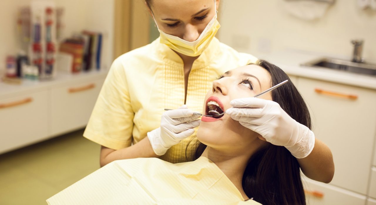 Dentista realizando diagnóstico de dentes de paciente. Seu uniforme é amarelo-claro.