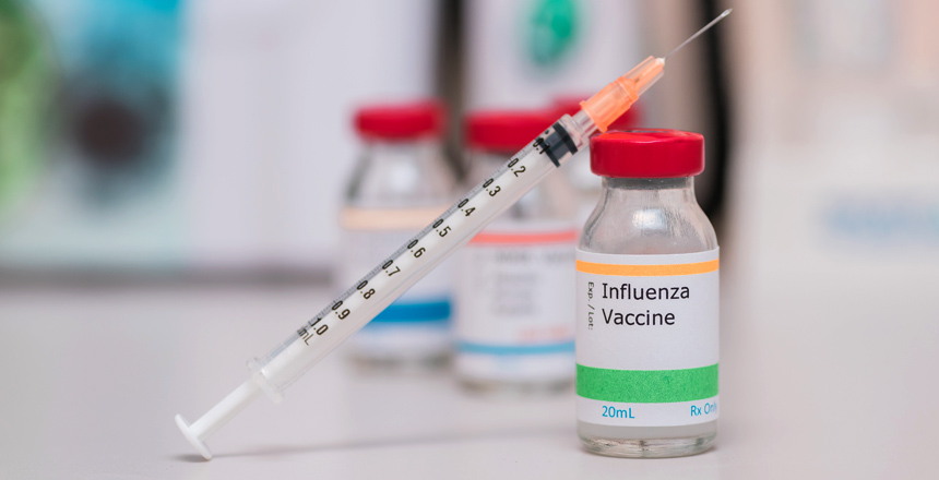 Frasco de Vacina contra influenza e pneumococos e seringa em cima.