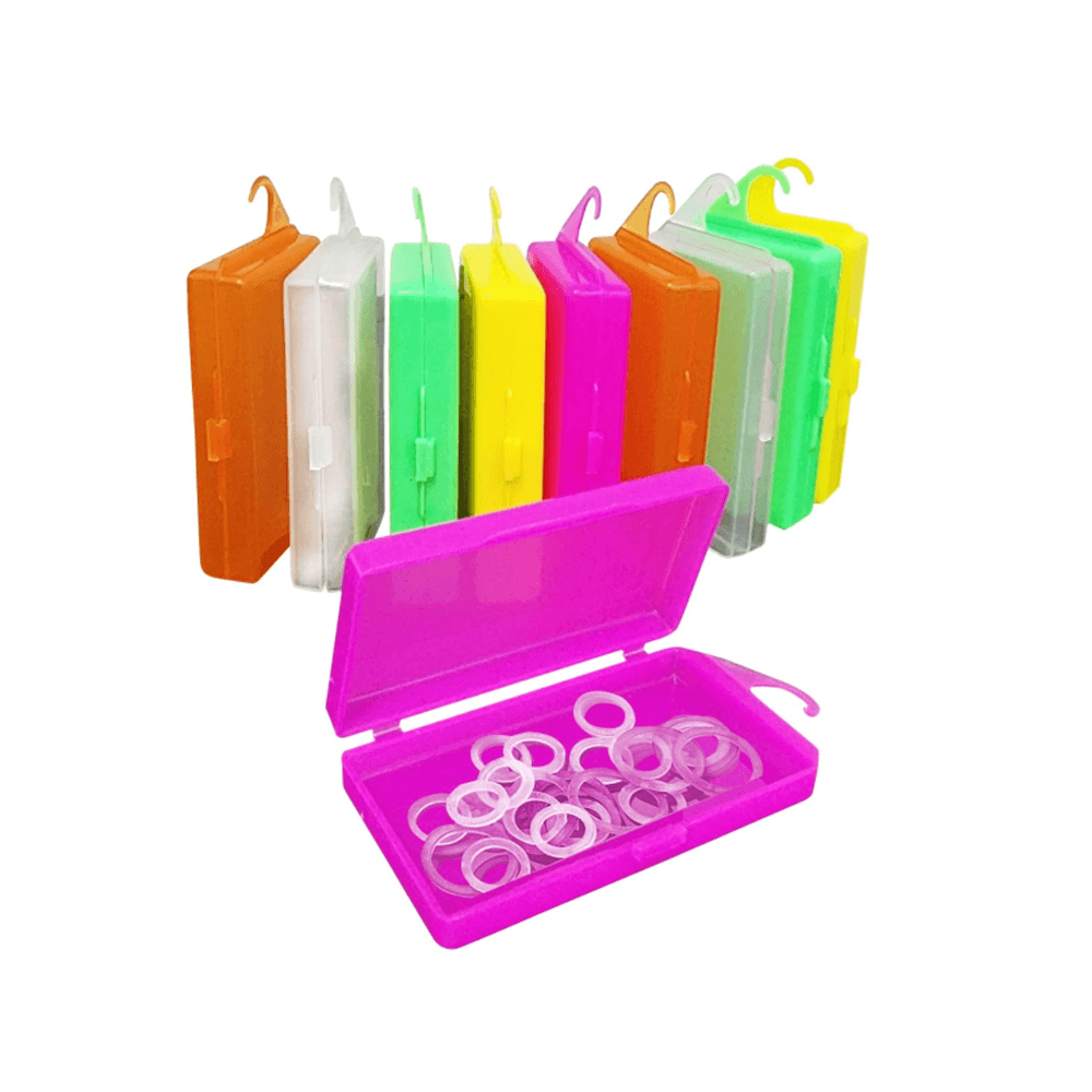 Na frente tem uma caixinha rosa aberta com vários elásticos ortodônticos dentro. Atrás tem várias outras caixnhas coloridas fechadas.