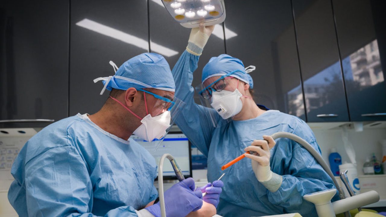 Dentista e assistente realizando procedimento. Ela está ajustando a luz.