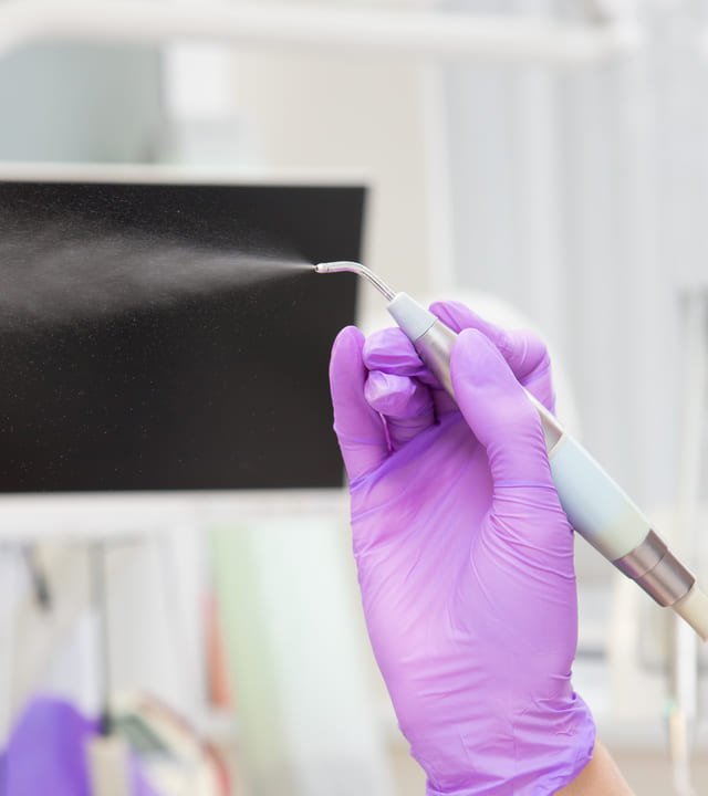 Dentista usando luvas roxas está segurando instrumento de jato de bicarbonato que está ligado.