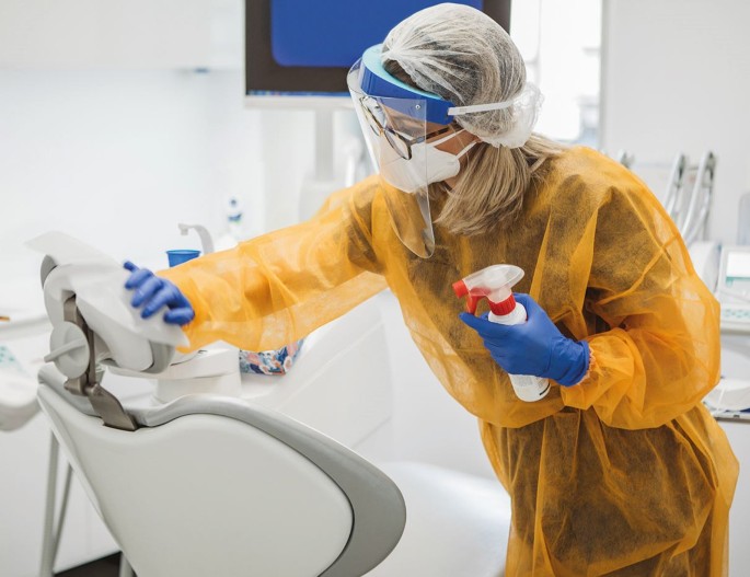 Dentista usando EPIS está limpando cadeira odontológico.