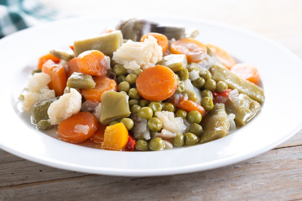 Prato branco fundo com vários legumes cozidos, como cenoura, couve-flor, abóbora, ervilhas e mais.