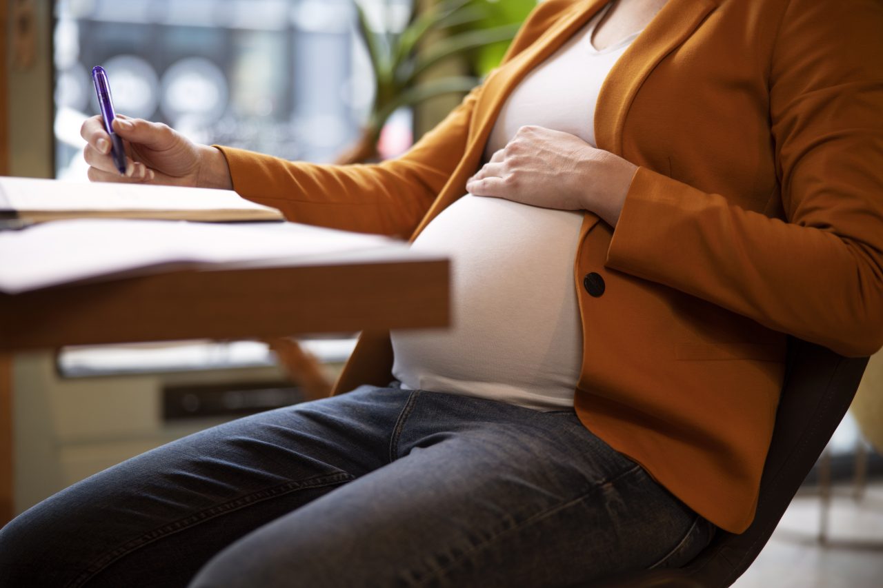 grávida está sentada em frente a mesa anotando em caderno