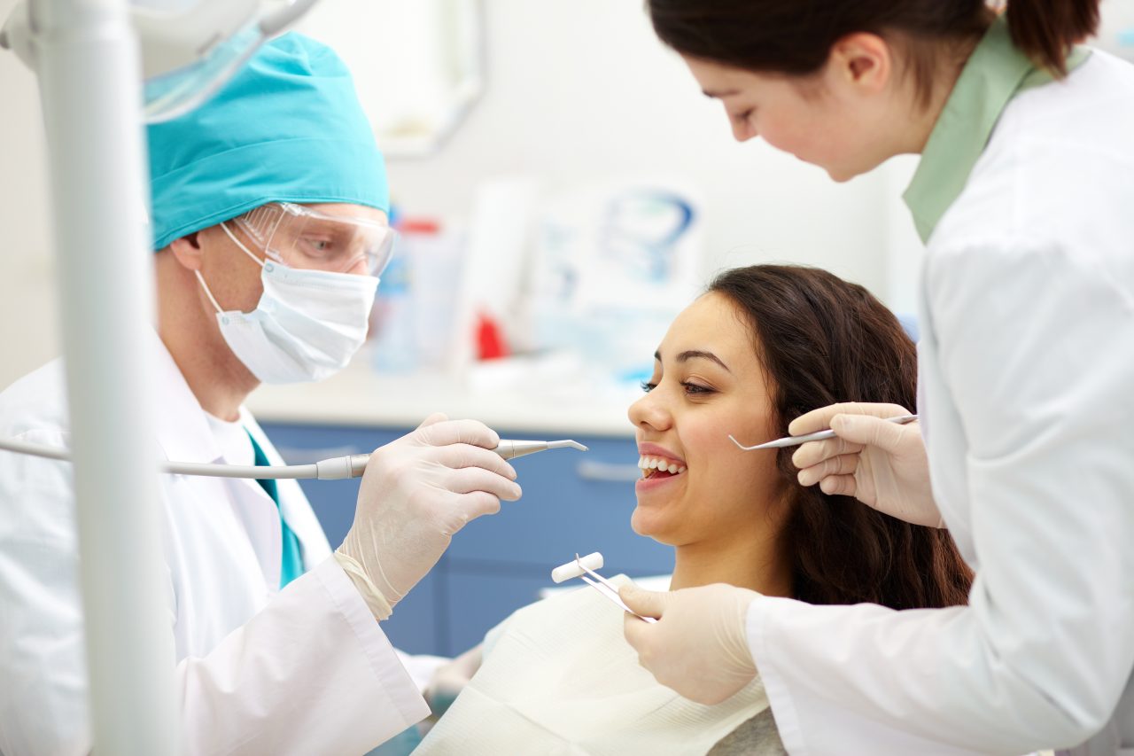 Dentista e sua assistente tratando paciente no consultório.