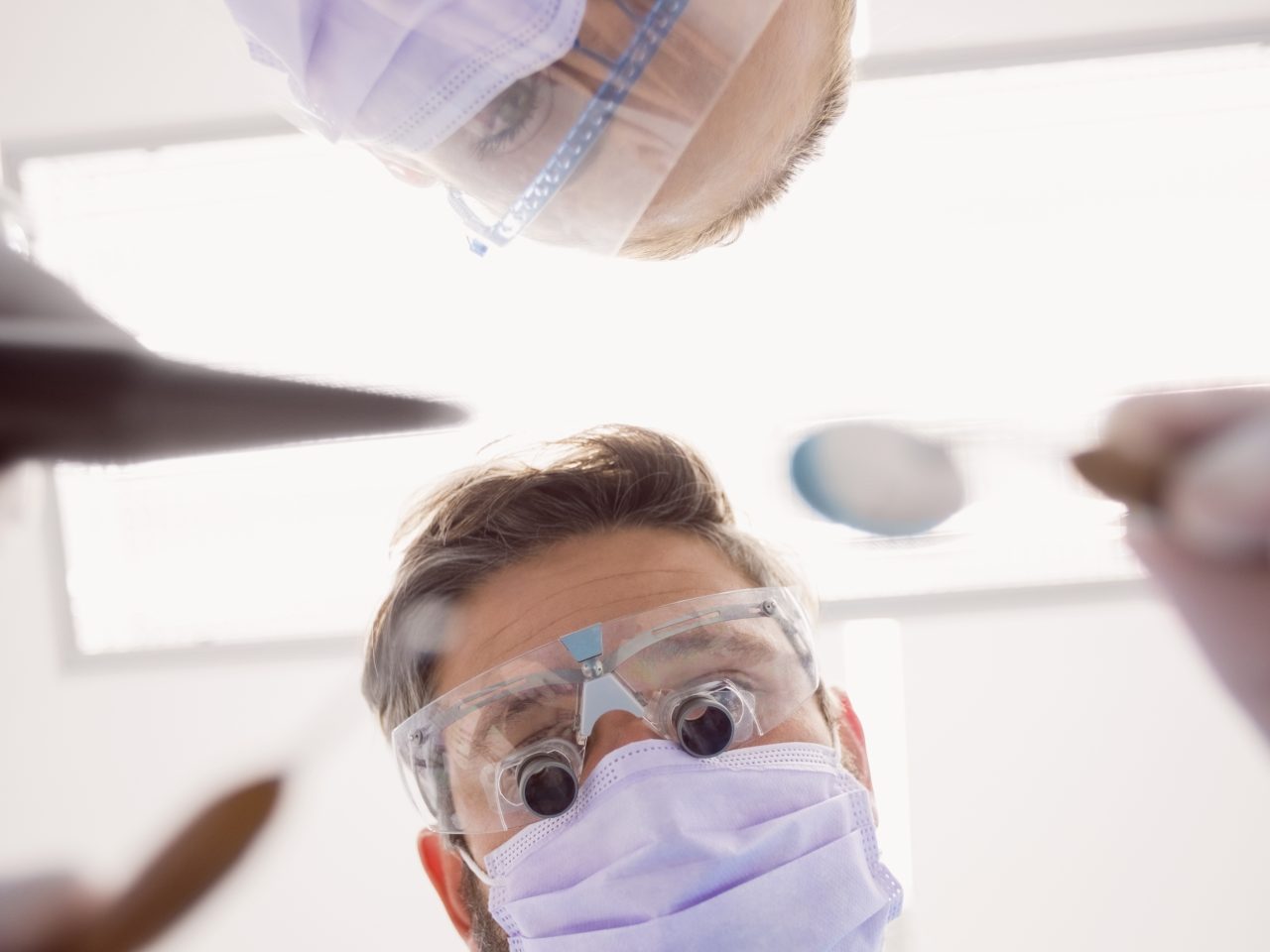 Imagem de ângulo baixo mostra dentista e assistente olhando para baixo com espelhinho na mão