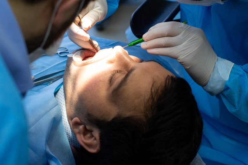 Dentista e assistente realizando cirurgia em dente de paciente