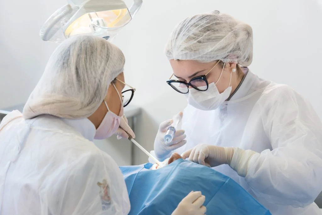 Dentista e assistente com seringa na mão durante atendimento.