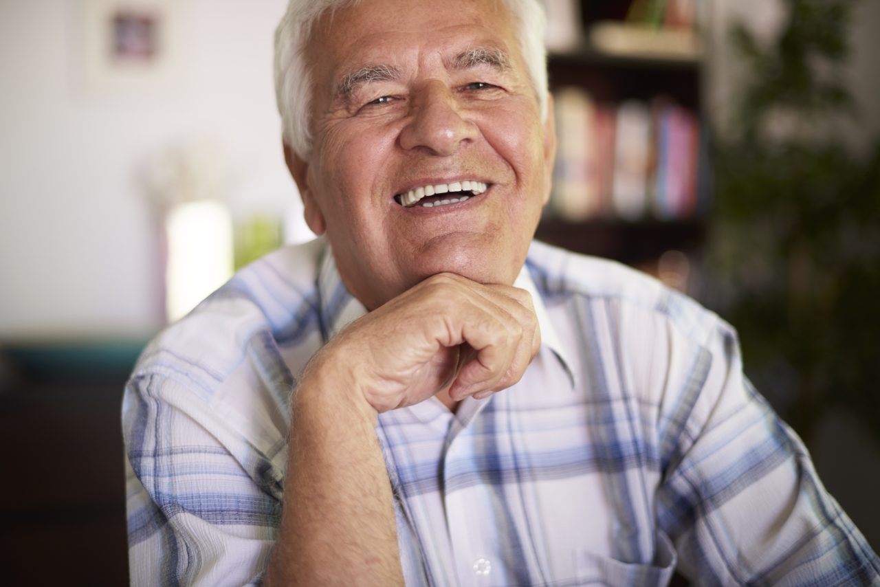 Senhor sorrindo, está sentado em casa.