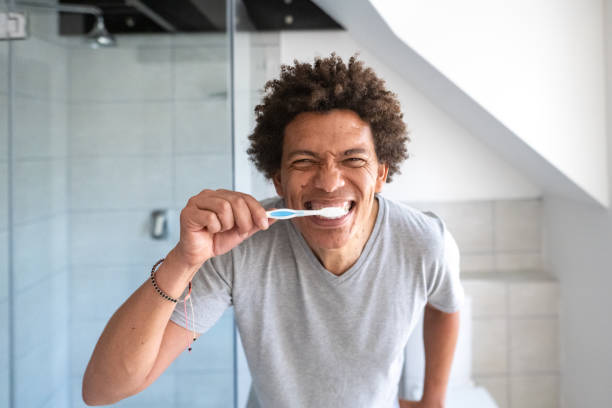 Homem escovando os dentes em frente ao espelho.
