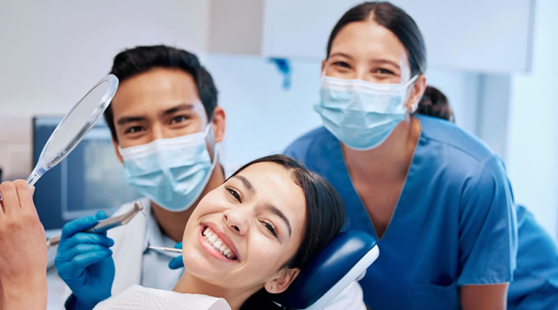 Dentista e assistente posando para foto com a paciente, todos estão com expressões sorridentes.