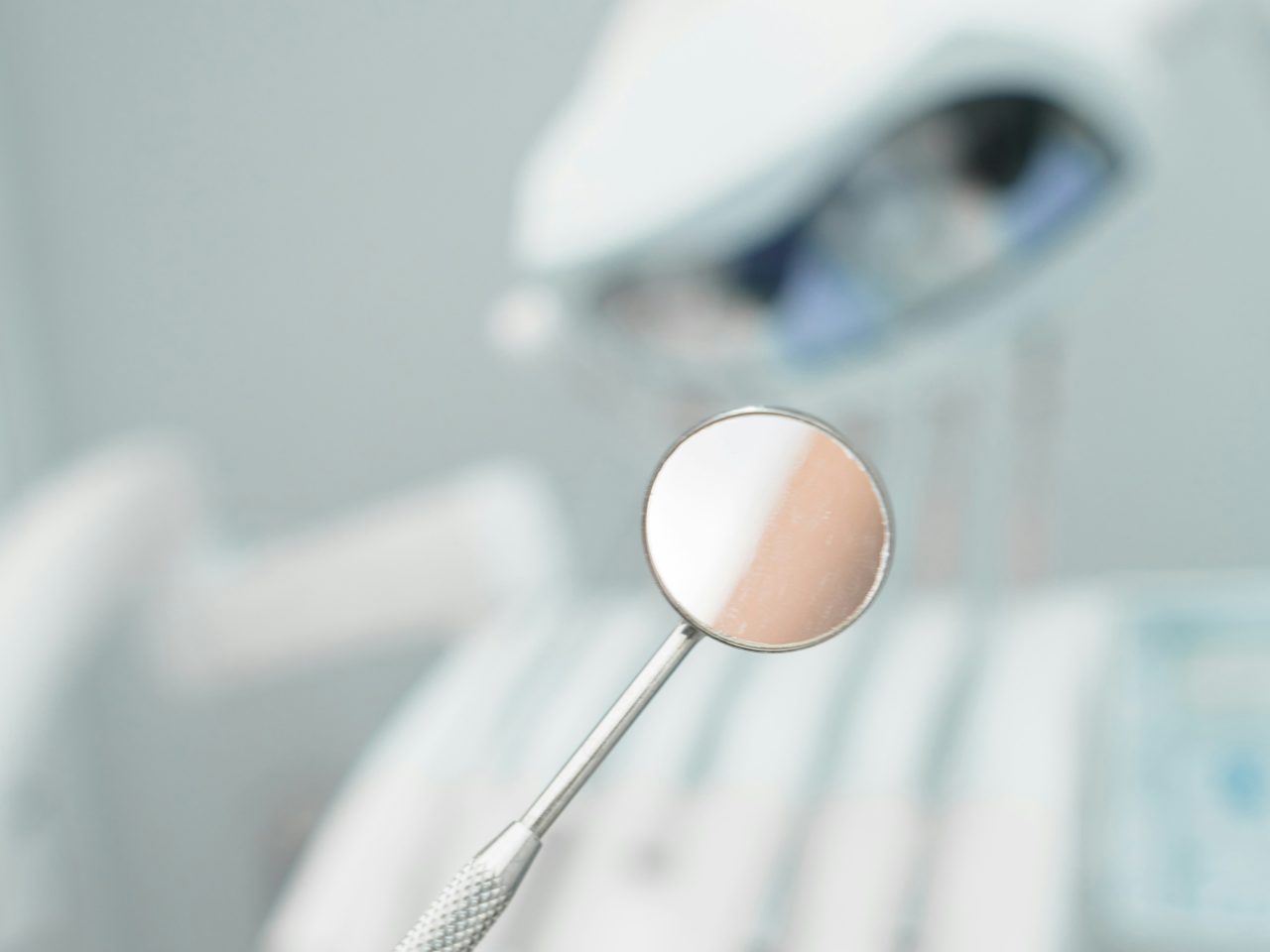 imagem focada em um espelhinho de dentista, o fundo desfocado é um consultório.