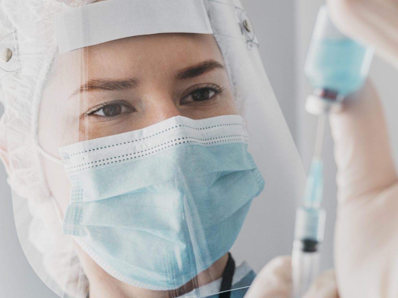 Doutora retirando com seringa líquido azul de frasco.