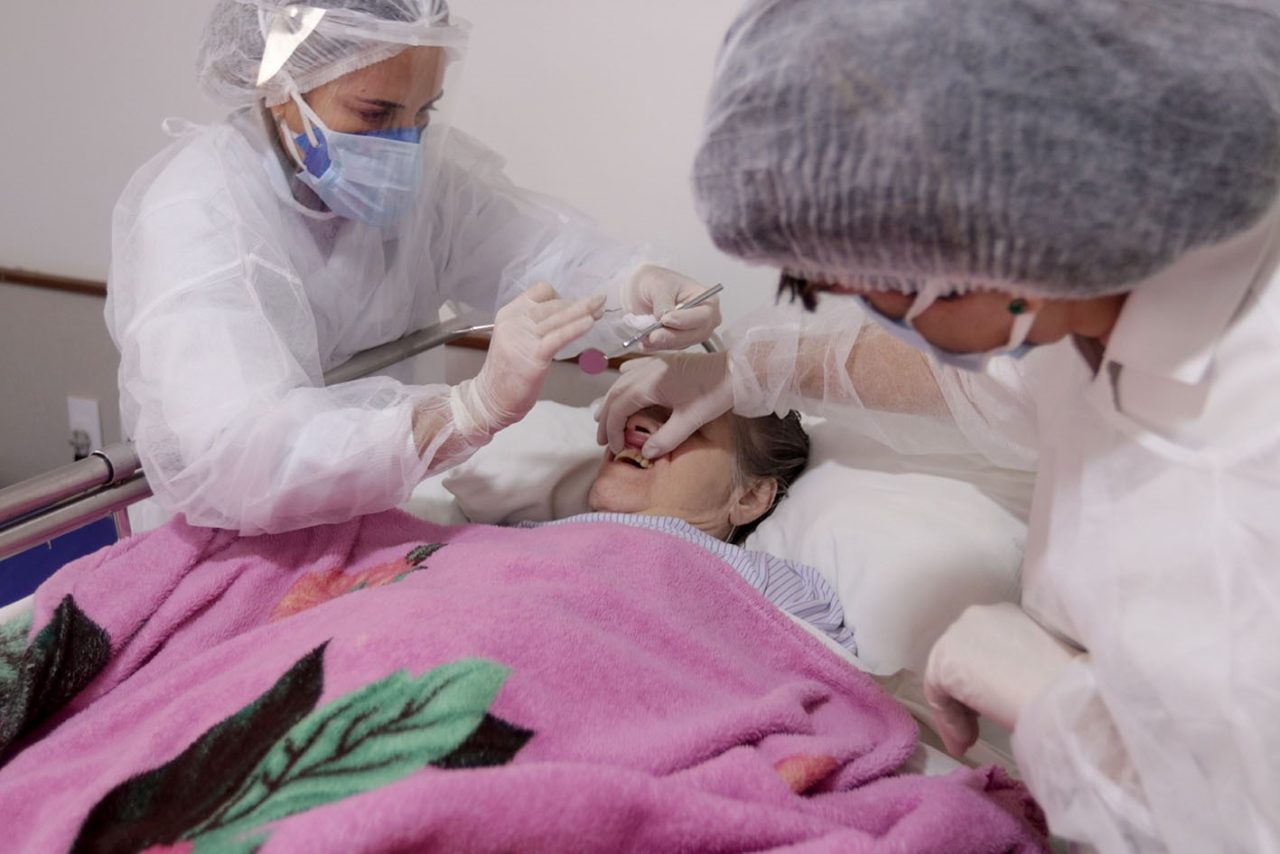 Dentista e assistente estão atendendo paciente acamada.