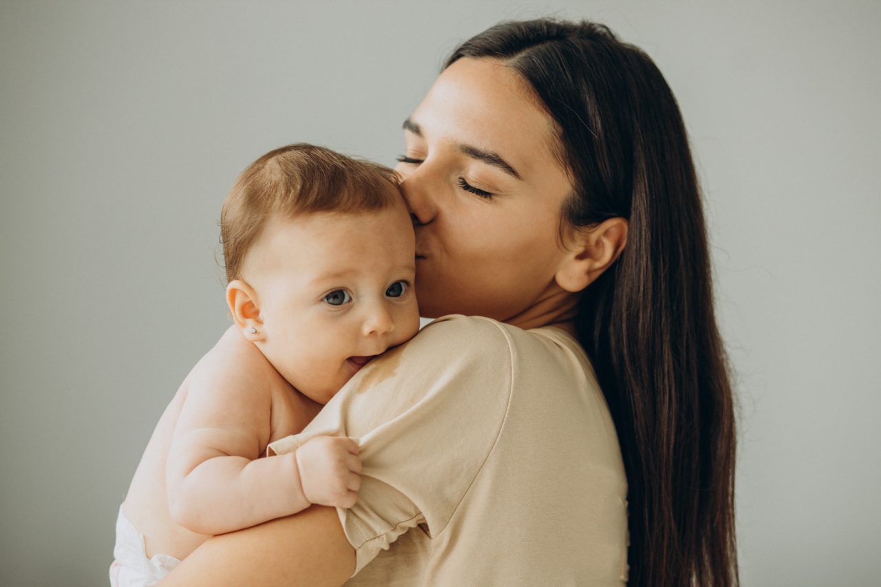 Mãe segurando sua filha bebê no colo e beijando sua testa.