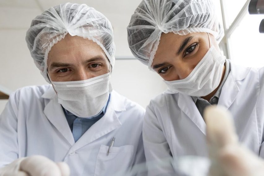 Dentista e assistente tratando de paciente. A imagem é tirada do ponto de vista do paciente, mostrando apenas o rosto dos profissionais de saúde.