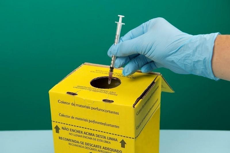 Descartando seringa em lixo coletor de materiais perfurocortantes.