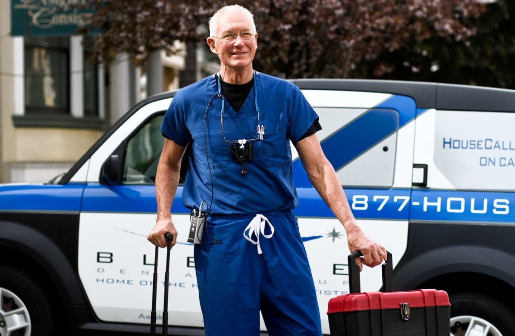 Dentista senhor está saindo de carro com maletas para atendimento odontológico domiciliar.