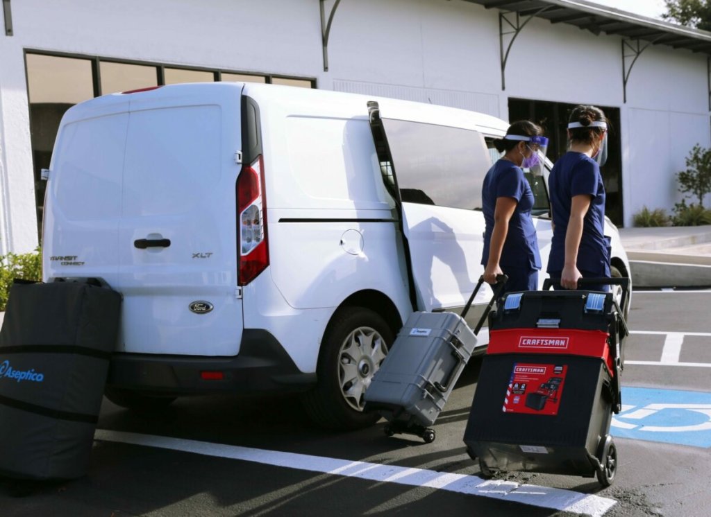 Duas dentistas desceram de van com maleta para realizar atendimento de odontologia domiciliar.