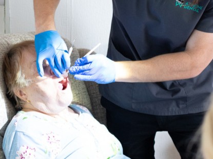 Dentista atendendo de forma domiciliar idosa que está sentada no sofá.