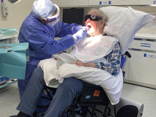 Senhor idoso de cadeiras de rodas está sendo atendido em consultório odontológico.