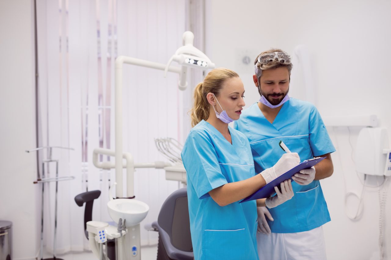 Dentista assinando algo em prancheta que seu assistente segura.