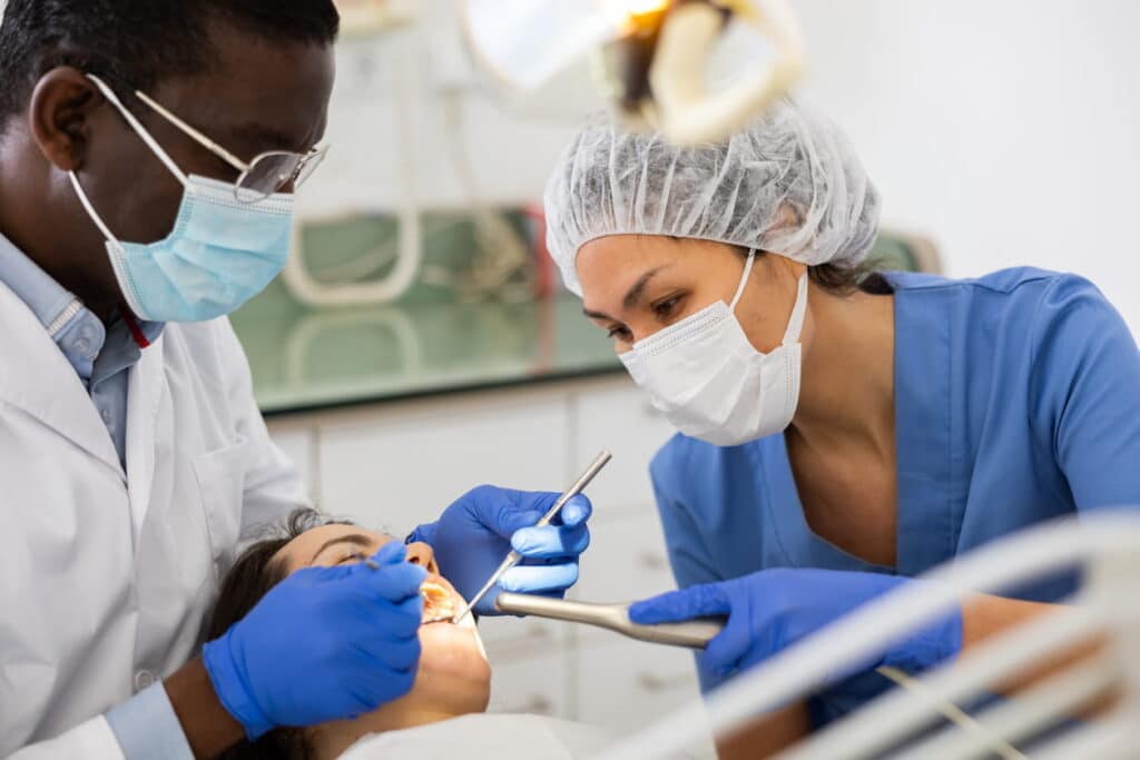 Dentista e auxiliar realizando limpeza em dente de paciente.