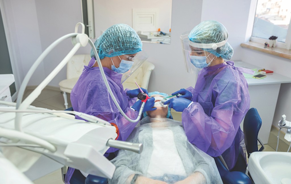 Dentista e técnica em saúde bucal atendendo paciente.